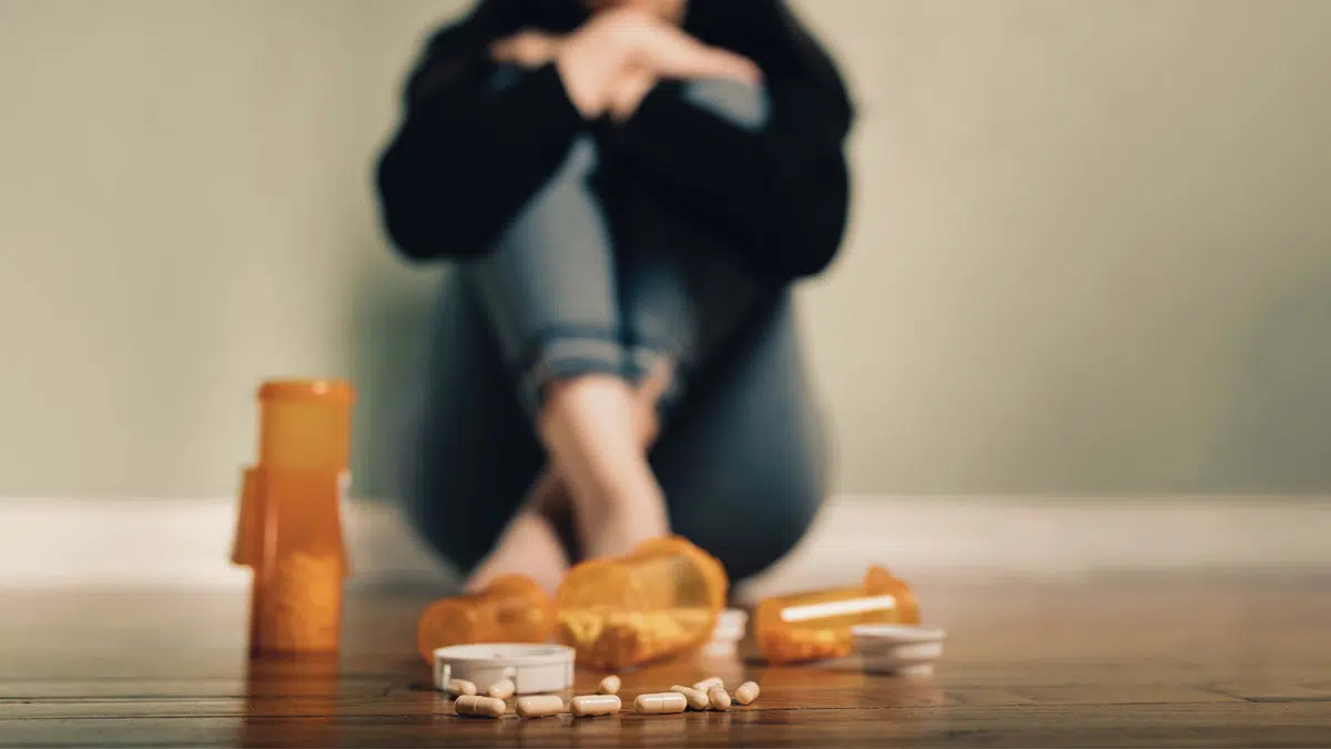 Woman sitting on the floor with several open pill bottles in front of her. Text describes the relationship between anxiety and addiction.